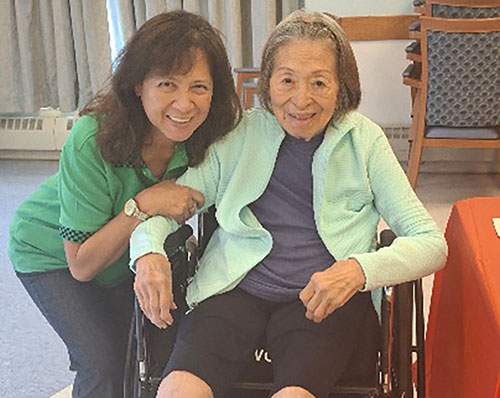Elderly woman in a wheelchair smiling with her adult daughter next to her also smiling
